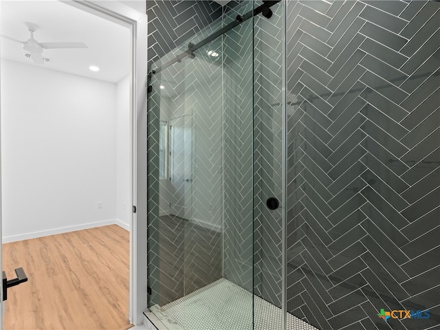 bathroom with a stall shower, ceiling fan, baseboards, and wood finished floors