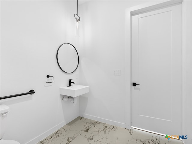 half bath with toilet, marble finish floor, baseboards, and a sink