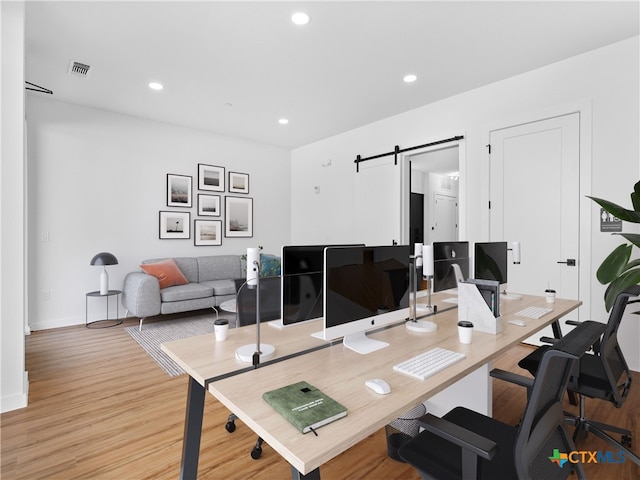 home office featuring a barn door, visible vents, baseboards, light wood-style floors, and recessed lighting