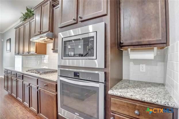 1400 Little Elm Trl Unit 1215, Cedar Park, TX 78613 - kitchen with stainless steel appliances, tasteful backsplash, light wood-style flooring, under cabinet range hood, and crown molding