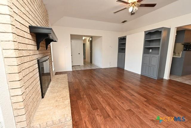 unfurnished living room with a fireplace, ceiling fan, built in features, and hardwood / wood-style flooring