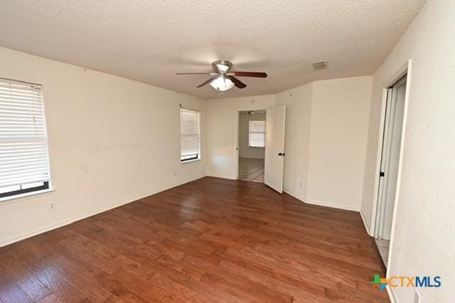 unfurnished room with ceiling fan, a healthy amount of sunlight, a textured ceiling, and dark wood-type flooring