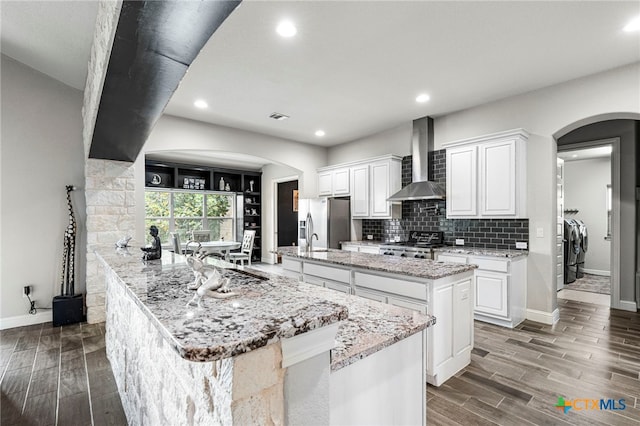 kitchen featuring stove, white cabinets, wall chimney range hood, a large island, and washing machine and clothes dryer