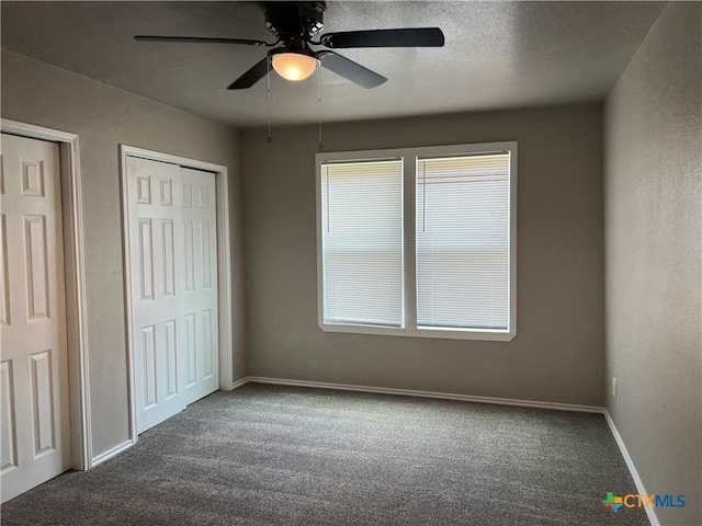 unfurnished bedroom featuring a textured ceiling, multiple closets, ceiling fan, and dark carpet