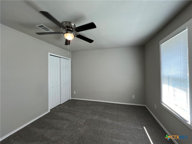 unfurnished bedroom featuring a textured ceiling, dark colored carpet, ceiling fan, and a closet