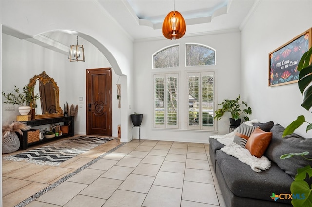 tiled entrance foyer featuring crown molding, a notable chandelier, a high ceiling, and a tray ceiling