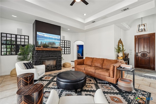 tiled living room featuring a stone fireplace, a towering ceiling, and ceiling fan