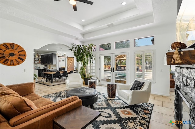 tiled living room with sink, ceiling fan, a tray ceiling, a fireplace, and a high ceiling