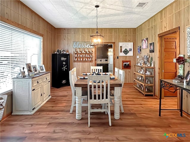 dining area featuring wood walls, light hardwood / wood-style floors, and a chandelier