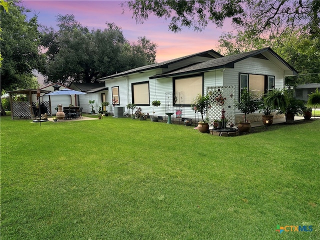 back house at dusk with a lawn, cooling unit, and an outdoor fire pit