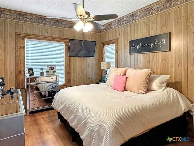 bedroom with hardwood / wood-style floors, ceiling fan, and wooden walls