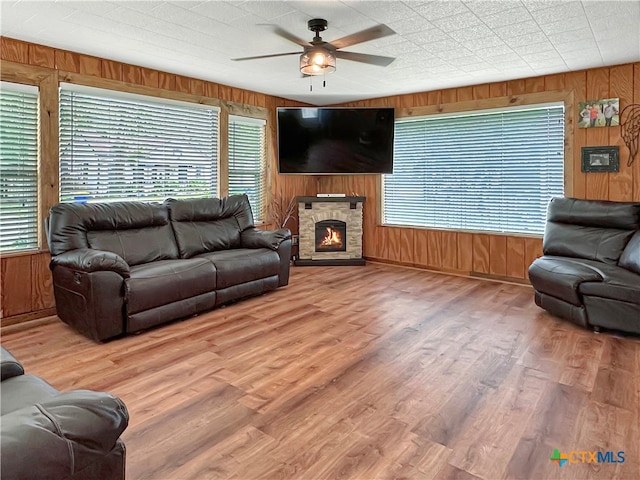 living room with wood walls, wood-type flooring, a fireplace, and ceiling fan