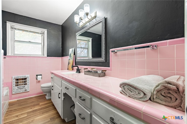 bathroom with heating unit, wood-type flooring, vanity, toilet, and tile walls