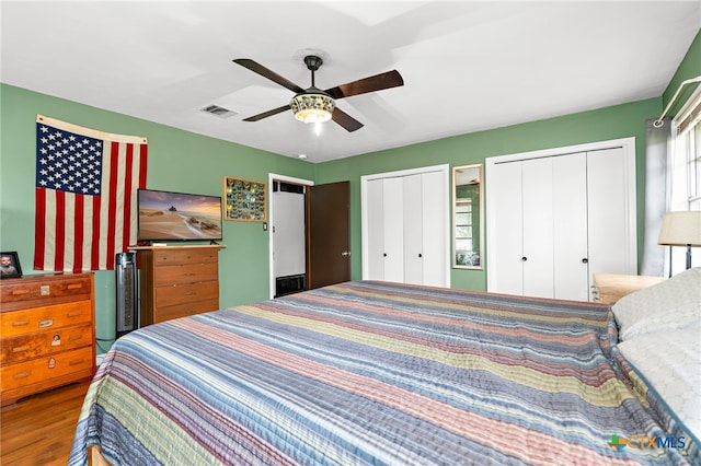 bedroom featuring hardwood / wood-style floors, two closets, and ceiling fan