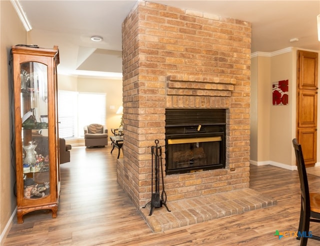 living room with wood-type flooring, ornamental molding, and a brick fireplace