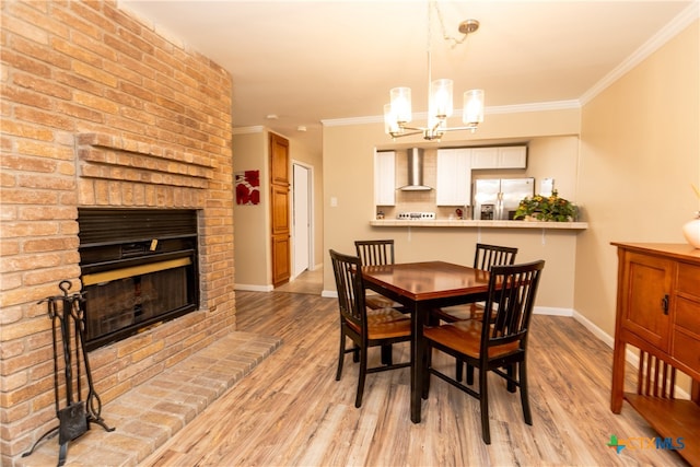 dining room featuring a brick fireplace, light hardwood / wood-style floors, crown molding, and an inviting chandelier