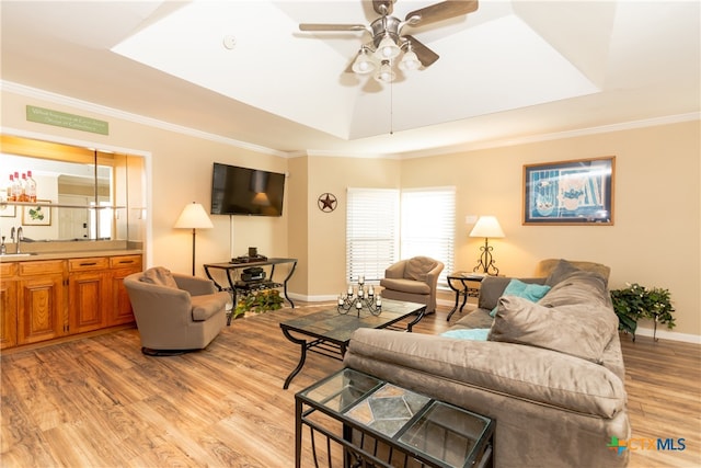 living room featuring ornamental molding, light hardwood / wood-style flooring, sink, and a raised ceiling