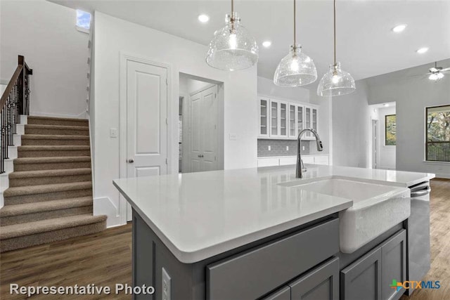 kitchen featuring dark hardwood / wood-style flooring, a center island with sink, hanging light fixtures, and gray cabinetry