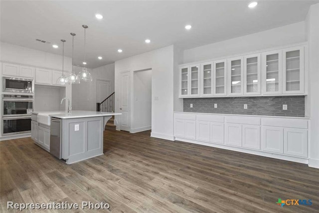 kitchen with a center island with sink, hanging light fixtures, dark hardwood / wood-style flooring, white cabinetry, and stainless steel appliances