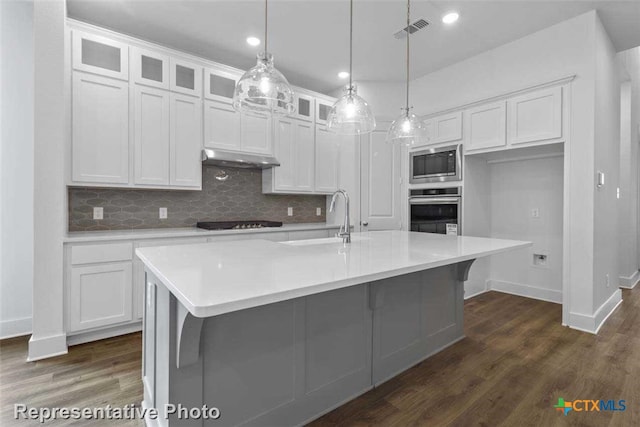 kitchen featuring appliances with stainless steel finishes, dark wood-type flooring, sink, a center island with sink, and white cabinets