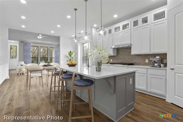 kitchen with ceiling fan, dark wood-type flooring, decorative light fixtures, a center island with sink, and white cabinetry