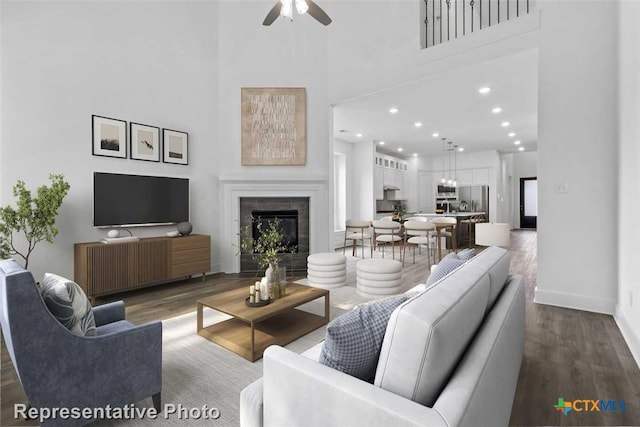 living room with a tile fireplace, a high ceiling, dark hardwood / wood-style flooring, and ceiling fan