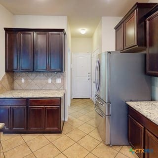 5120 Siltstone Loop, Killeen, TX 76542 - kitchen with freestanding refrigerator, backsplash, light tile patterned floors, and light stone counters