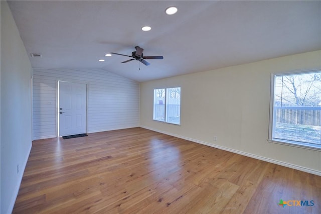 spare room with ceiling fan, wooden walls, light hardwood / wood-style floors, and vaulted ceiling