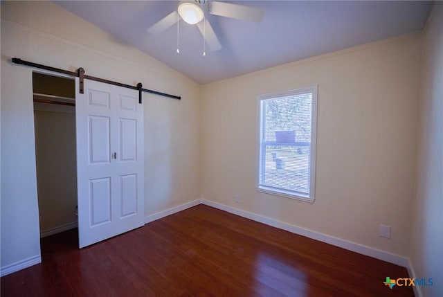 unfurnished bedroom with ceiling fan, a barn door, dark hardwood / wood-style floors, a closet, and lofted ceiling