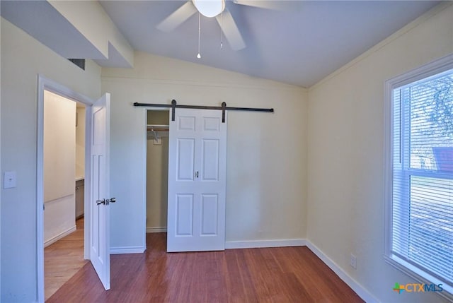 unfurnished bedroom featuring hardwood / wood-style floors, lofted ceiling, ceiling fan, a barn door, and a closet