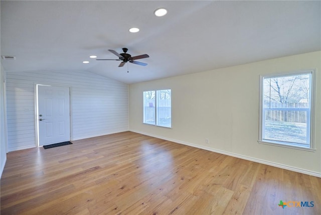 unfurnished room featuring light wood-type flooring, vaulted ceiling, ceiling fan, and wooden walls