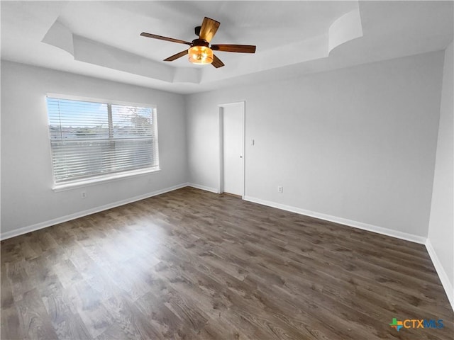 empty room with a tray ceiling, ceiling fan, and dark hardwood / wood-style flooring