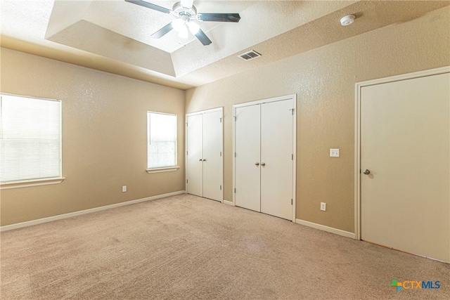 unfurnished bedroom with multiple closets, light colored carpet, ceiling fan, and a raised ceiling