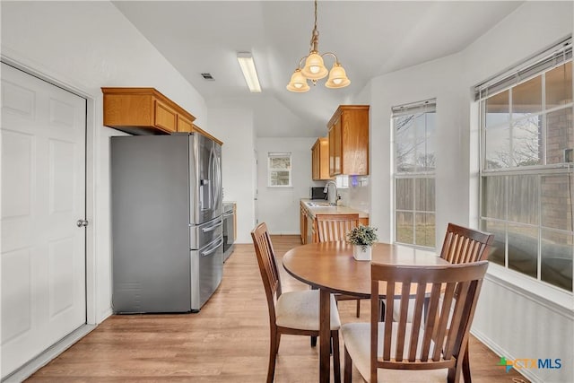 dining area featuring a healthy amount of sunlight, sink, a chandelier, and light wood-type flooring