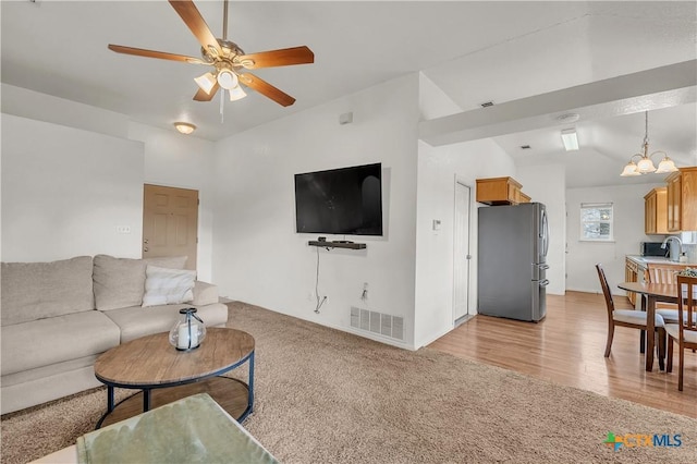 carpeted living room featuring ceiling fan with notable chandelier, sink, and vaulted ceiling