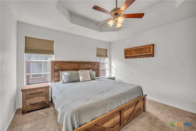 bedroom with ceiling fan, light colored carpet, multiple windows, and a tray ceiling