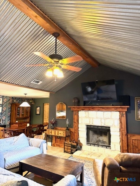 living area with a stone fireplace, vaulted ceiling with beams, and a ceiling fan