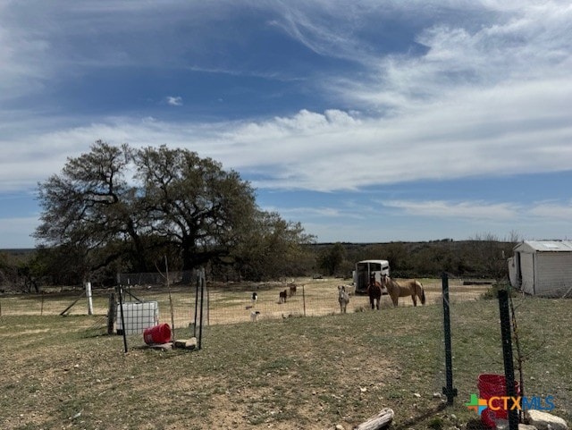 view of yard featuring an outdoor structure, a storage unit, a rural view, and fence