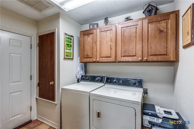 clothes washing area with a textured ceiling, washer and clothes dryer, and cabinets