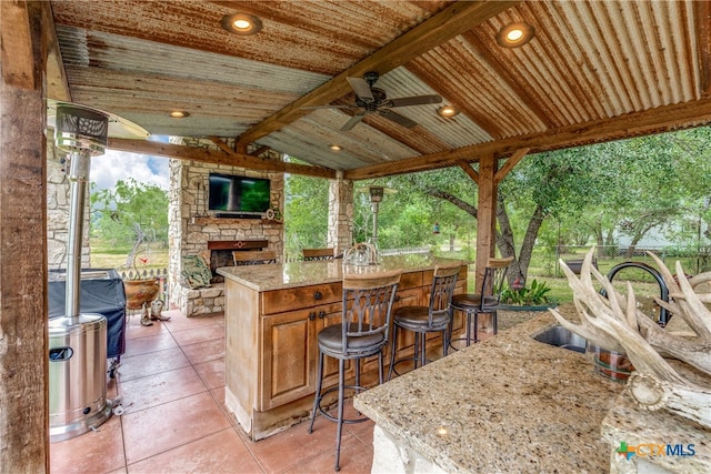 view of patio featuring an outdoor stone fireplace, an outdoor bar, and ceiling fan