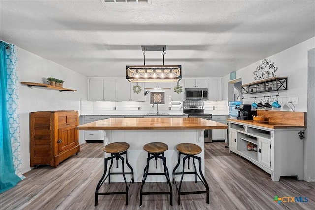 kitchen featuring backsplash, hanging light fixtures, white cabinets, and stainless steel appliances