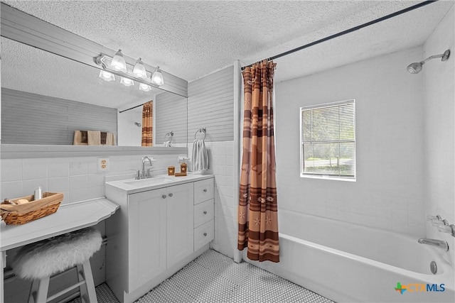 bathroom featuring a textured ceiling, shower / tub combo with curtain, vanity, and tile walls