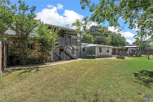 back of house featuring ceiling fan, a yard, and a fire pit