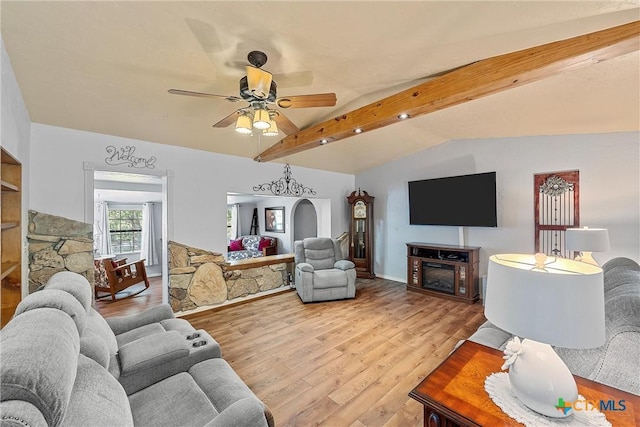 living room featuring lofted ceiling with beams, ceiling fan, a stone fireplace, and light wood-type flooring