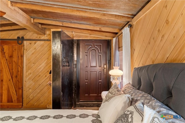 bedroom with vaulted ceiling with beams, a barn door, wooden ceiling, and wood walls