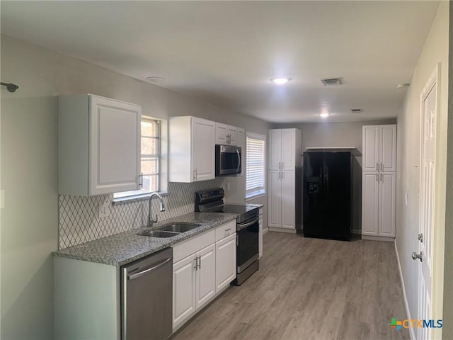 kitchen featuring sink, white cabinetry, light wood-type flooring, appliances with stainless steel finishes, and decorative backsplash