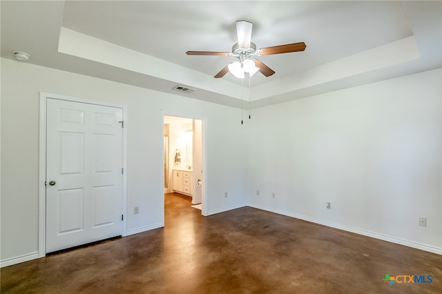 unfurnished bedroom featuring ceiling fan, ensuite bath, and a tray ceiling