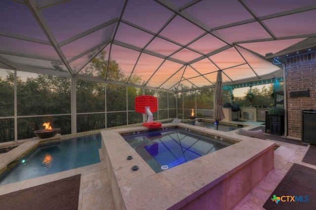 pool at dusk with an outdoor kitchen, an in ground hot tub, a lanai, an outdoor fire pit, and a patio area