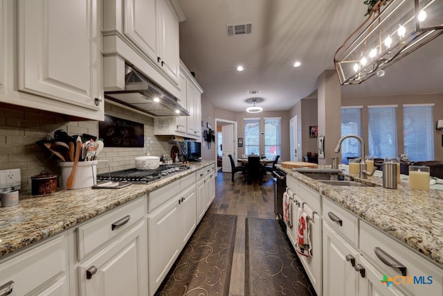 kitchen with stainless steel gas cooktop, sink, white cabinetry, hanging light fixtures, and light stone countertops