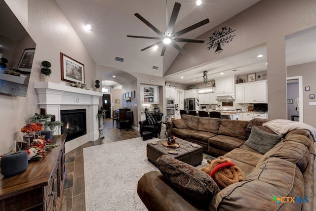 living room with a premium fireplace, high vaulted ceiling, ceiling fan, and light hardwood / wood-style flooring